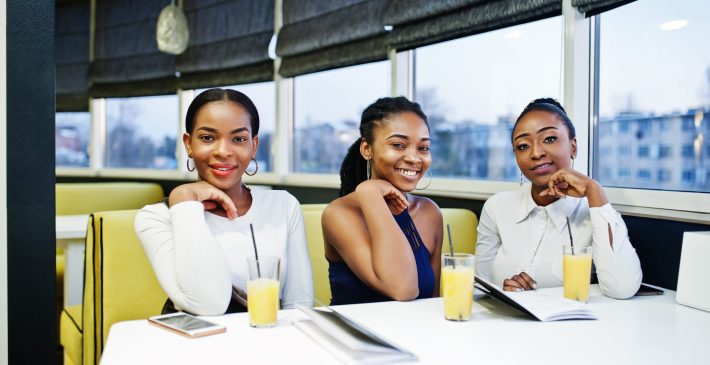 Three african woman in dress posing at restaurant, read the menu Three african woman in dress posing at restaurant, read the menu.